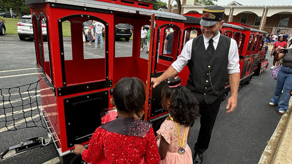 Maxi Express trackless train rented for an outdoor family event, boarding area filled with excited children and parents