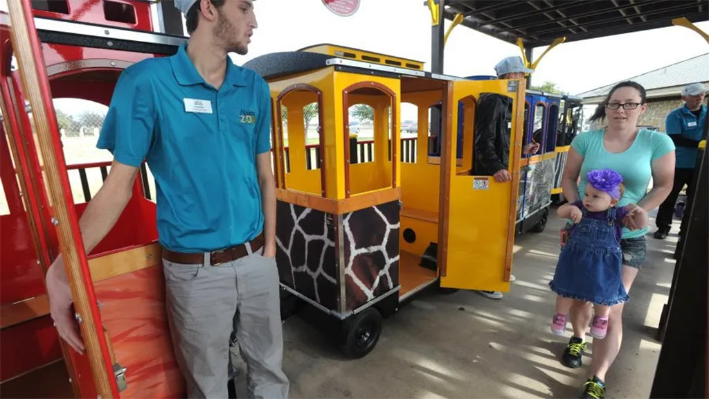 Wattman Maxi Express train driving past animal exhibits with children and parents on board in a busy zoo environment